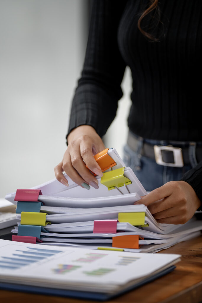 Kobieta segregująca dokumenty układając je w pliki i oznaczając kolorowymi znacznikami